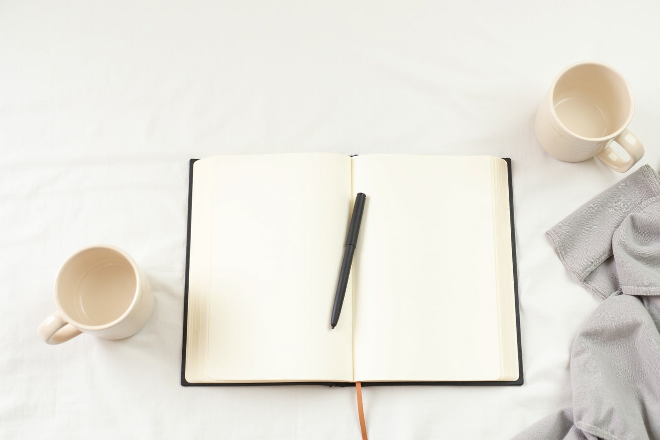 A minimal editorial flatlay of an open journal, pen, and mugs — birthday gifts for serious readers