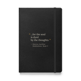 Black hardcover journal, front: “…for the soul is dyed by the thoughts.” Marcus Aurelius, quote marks in warm matte gold.