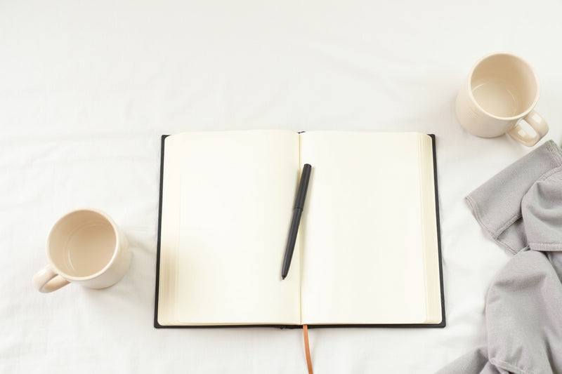 A minimal editorial flatlay of an open journal, pen, and mugs — birthday gifts for serious readers