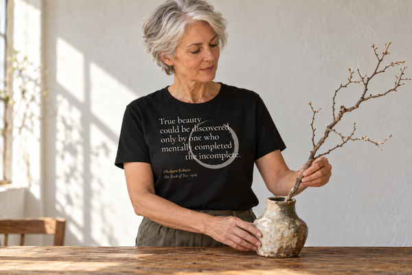 Woman placing a bare branch in a handmade vase, wearing the True Beauty — Okakura Kakuzō tee.